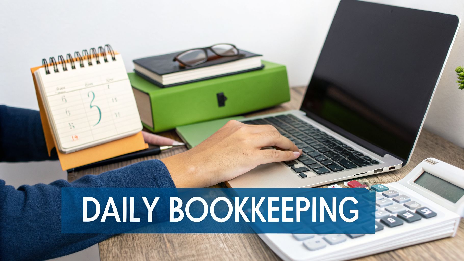 Person typing on a laptop at a desk with a calendar, books, and calculator, illustrating daily bookkeeping tasks.