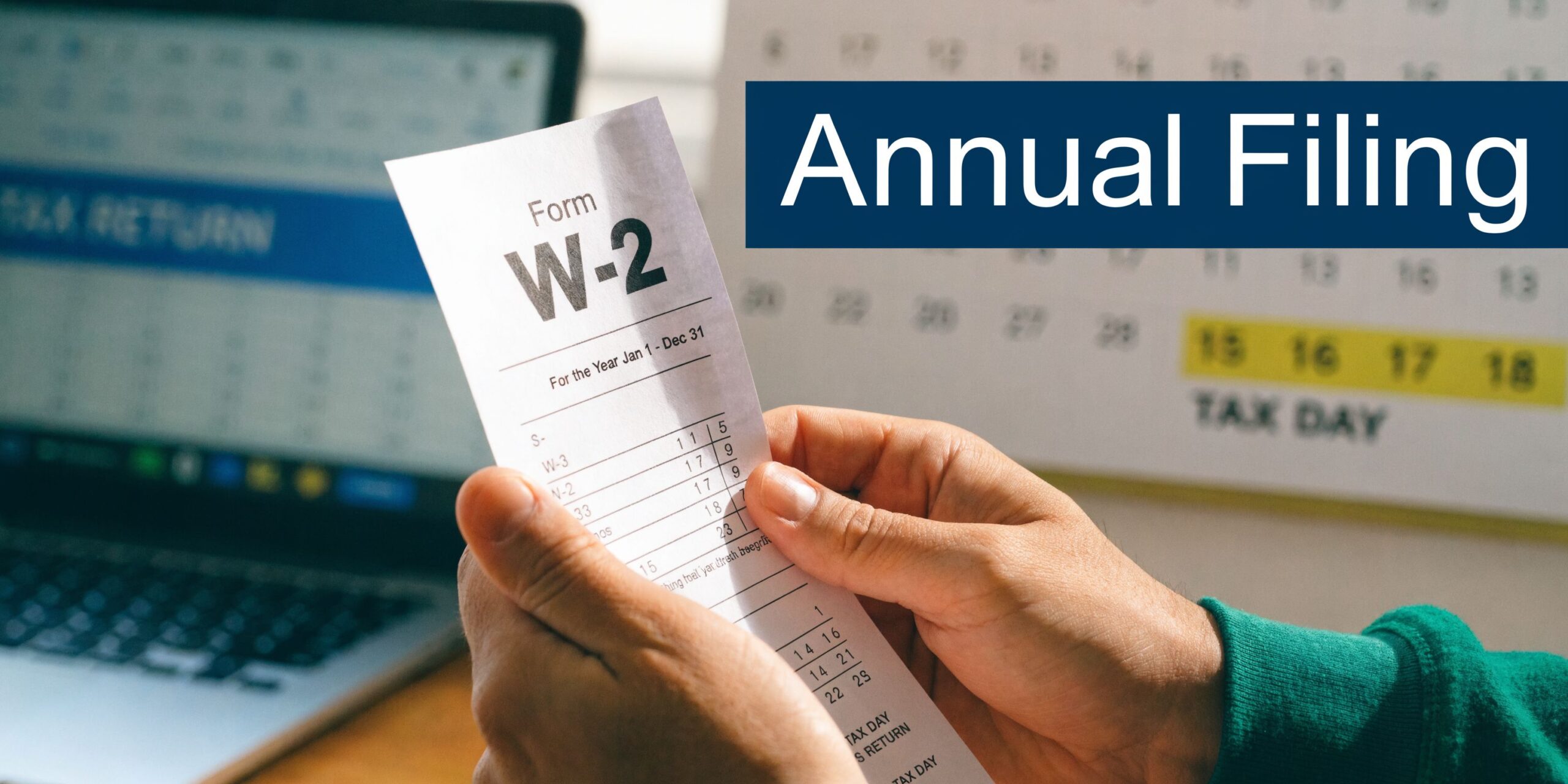 A person holding a W-2 form with a blurred laptop and a tax day calendar in the background.