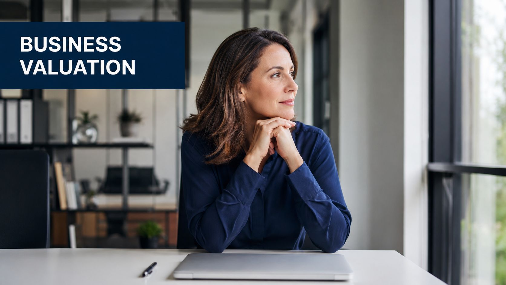 A professional woman in a dark blue shirt sitting at a desk, contemplating during business valuation